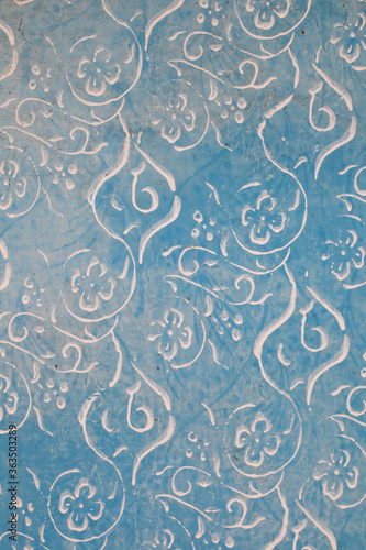Fragment starej, niebieskiej, wyblakłej ściany, pomalowany farbą kredową , ozdobiony kwiecistym wzorem.