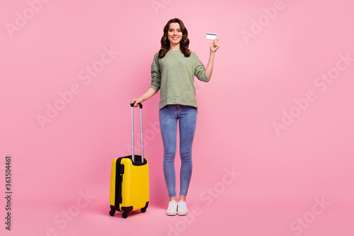 Full length photo of positive cheerful girl tourist ready leaving travel abroad hold yellow bright trolley plastic card wear green sweater isolated over pastel color background