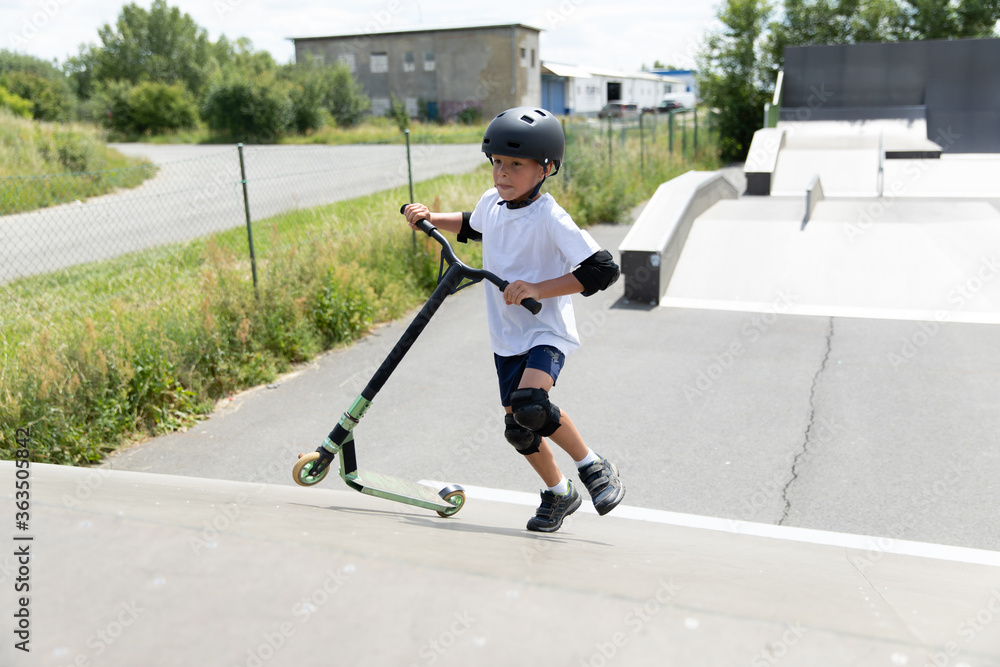 A cute little boy rides a scooter in a skatepark.