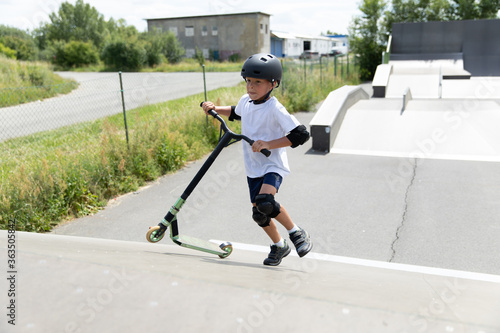 Obraz na płótnie A cute little boy rides a scooter in a skatepark. w salonie