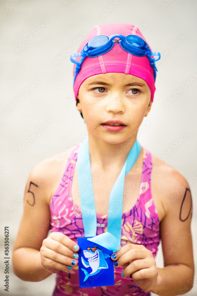 Vertical portrait of small tired 9 years old girl swimmer after finish on open water competition for children with medal. Sport and activity for kids. Swimming. Healthy lifestyle from childhood Vertical portrait of small tired 9 years old girl swimmer after finish on open water competition for children with medal. Sport and activity for kids. Swimming. Healthy lifestyle from childhood