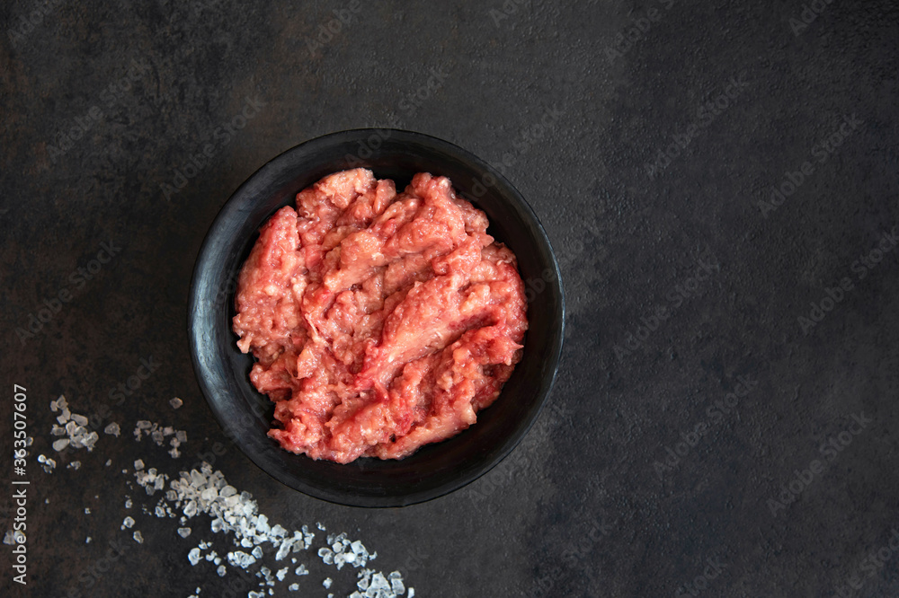 Homemade minced meat in a black bowl and salt on a black background. Fresh Raw mince. Top view with copy space Homemade minced meat in a black bowl and salt on a black background. Fresh Raw mince. Top view with copy space