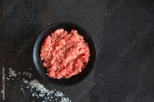 Homemade minced meat in a black bowl and salt on a black background. Fresh Raw mince. Top view with copy space