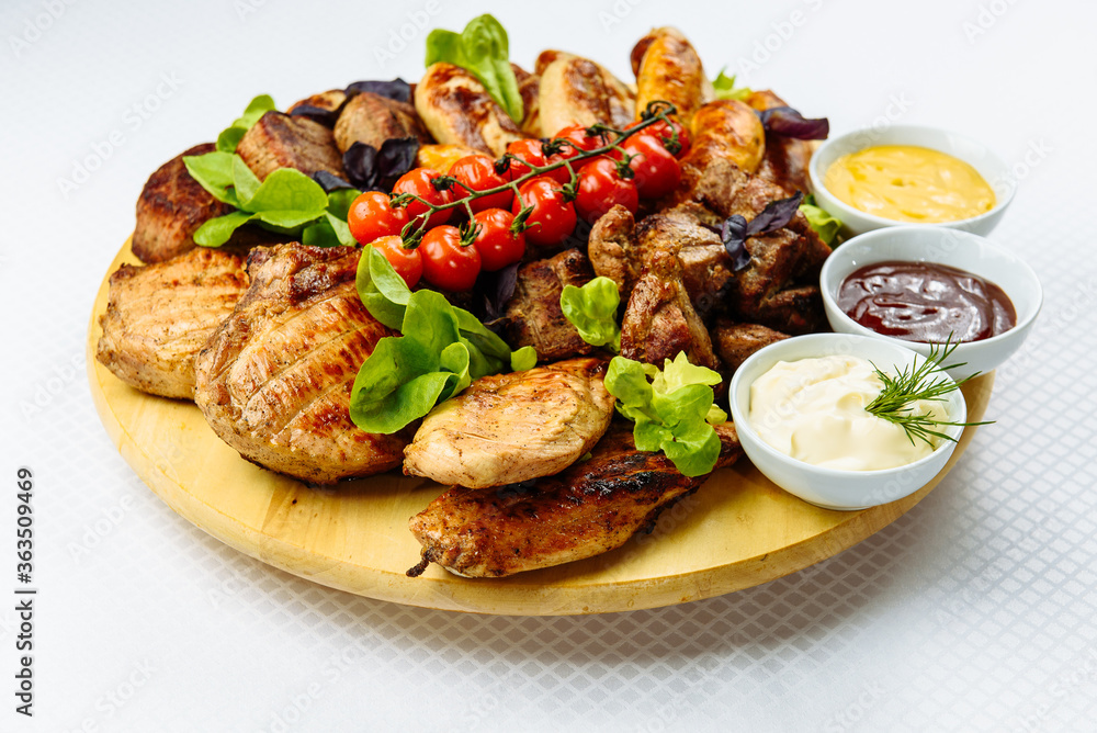 plate with fried meat, a wooden plate on a white tablecloth with fried meat, steak, barbecue, tomatoes and sauce plate with fried meat, a wooden plate on a white tablecloth with fried meat, steak, barbecue, tomatoes and sauce