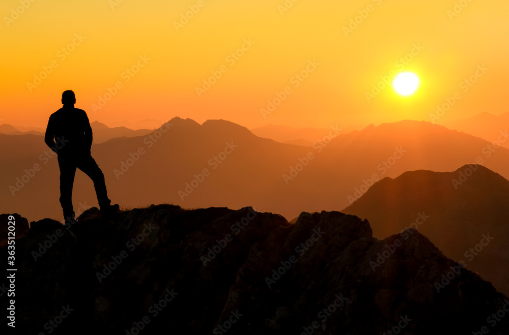 Happy success winning man standing relaxed on mountain at sunset. Border region of Tyrol, Austria and Allgaeu, Bavaria, Germany.