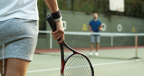 Happy young couple playing tennis on tennis court, close up view of hands with racket. © VAKSMANV