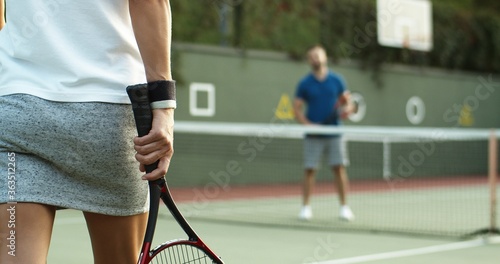 Rear of female tennis player walking at sport court to net where meeting with male co-player. Close up of racket in female hand. Back view. © VAKSMANV
