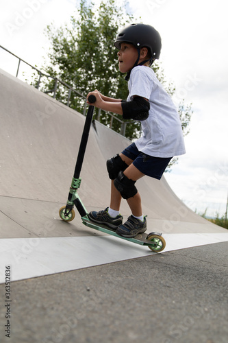 Obraz na płótnie A cute little boy rides a scooter in a skatepark. w salonie