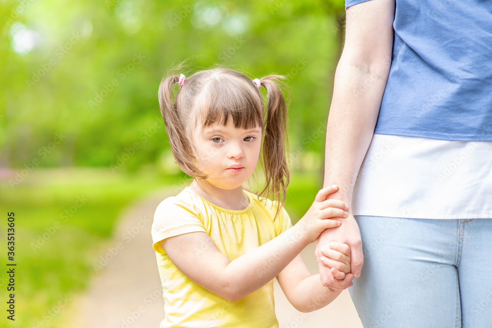 Happy little girl with syndrom down holds mom's hand in a sunny summer park. Empty space for text Happy little girl with syndrom down holds mom's hand in a sunny summer park. Empty space for text