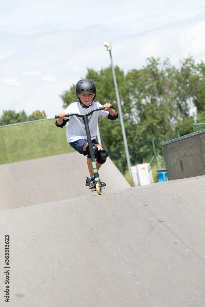 A cute little boy rides a scooter in a skatepark.