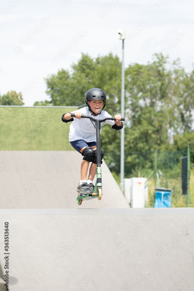 A cute little boy rides a scooter in a skatepark.