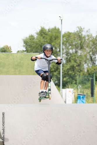 Obraz na płótnie A cute little boy rides a scooter in a skatepark. w salonie