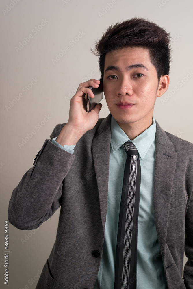Portrait of young handsome Asian businessman in suit talking on the phone Portrait of young handsome Asian businessman in suit talking on the phone