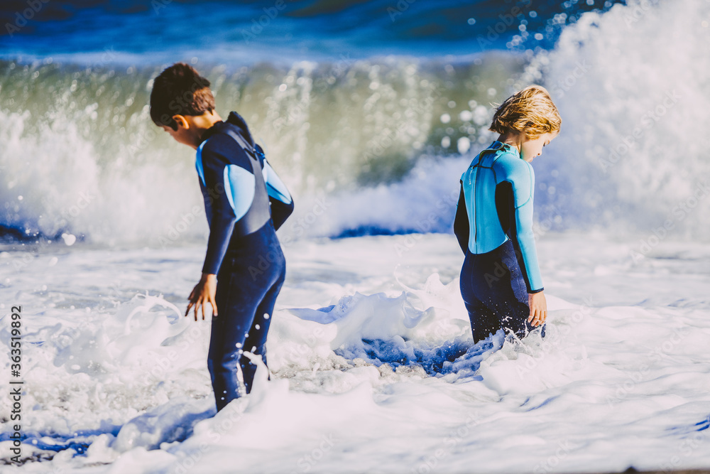 Two friends kids enjoying a funny surf day in the shore of a sunny beach in their coastal holidays 