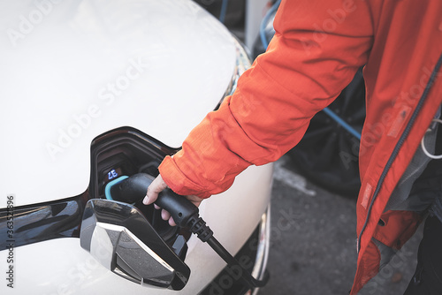 Human hand is holding Electric Car Charging connect to Electric car.