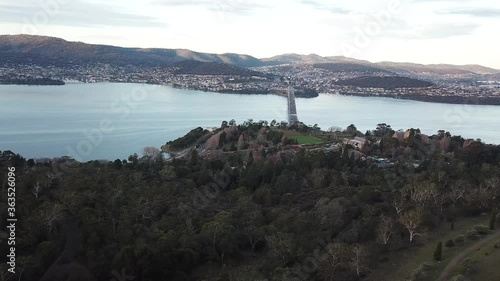 Aerial drone pan up to reveal busy bridge traffic during twilight afternoon surrounded by river with small mountains in background in Hobart, Tasmania, Australia. Derwent Bridge. photo