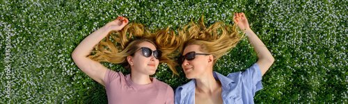 Fotografie Two young happy women in a flowery meadow on sunny day, top view, close-up
