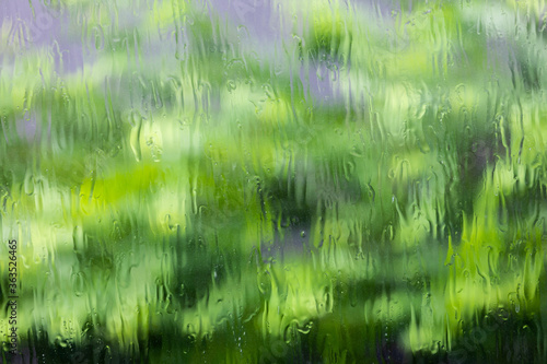 Water flowing on clear glass window with green background.