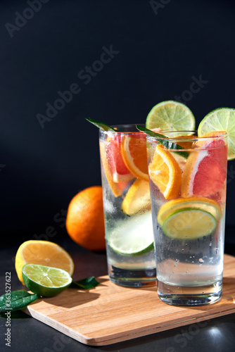 Health care  fitness  healthy nutrition diet concept. Fresh cool homemade citrus infused detox water with grapefruit  orange  lemon and lime and ice in glasses on dark background.