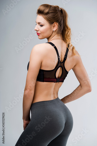Young happy fitness girl with sporty body drink at studio on a white background. Beautiful fit Girl. Fitness model in gray sportswear. Healthy lifestyle. © WellStock