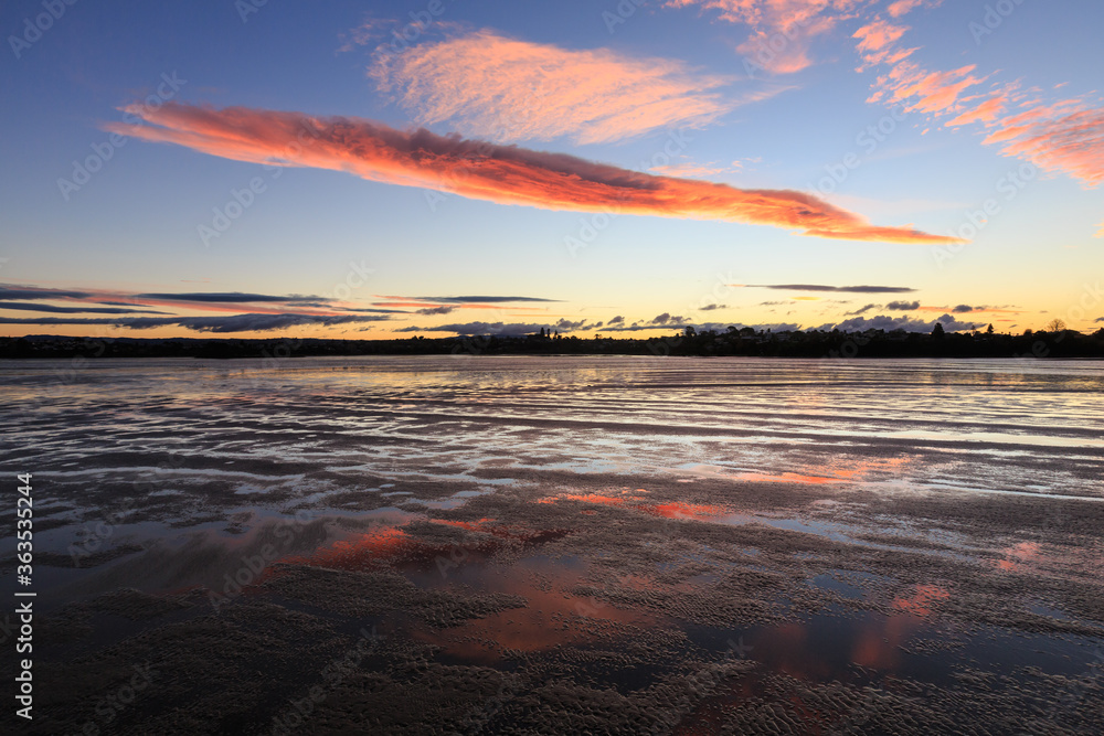 Sunset clouds reflected on the wet sand of a beach at low tide