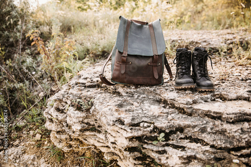 Canvastavla Black leather hiking boots and a vintage leather backpack, on a rock in mountains