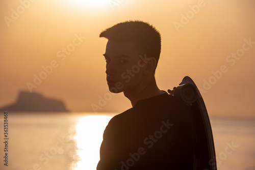 Teenager with his longboard at dawn near the ocean, sea © Chebix