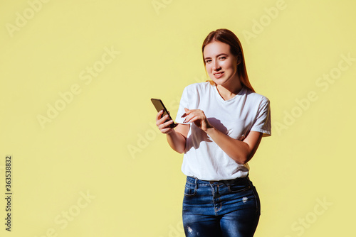 Pretty smiling woman using smartphone in city over yellow background