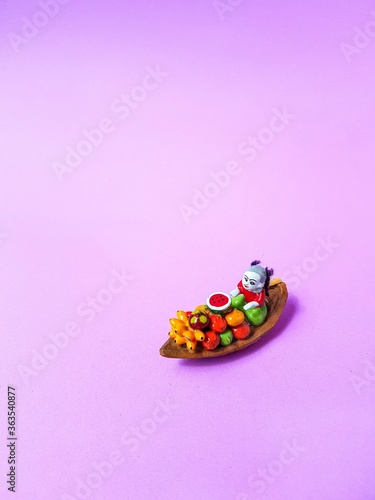 A traditional ceramic Thailand souvenir boat with fruit and a woman on a bright purple background.