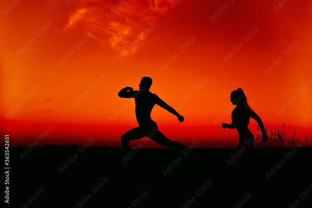 silhouettes of a couple running in nature in summer at sunset