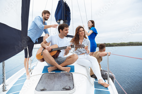 Group of happy friends drinking vodka cocktails at boat party outdoor, cheerful and happy. Young people playing guitar in sea tour, youth and summer vacation concept. Alcohol, vacation, resting. © master1305