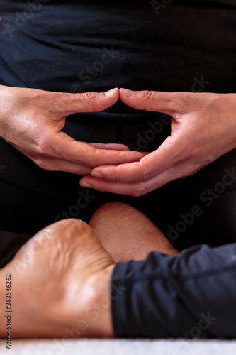 Yoguini making contemplative hand gesture Dhyana Mudra during meditation exercise  hands placed on the lap and palms facing upward. Vertical detail of hands and feet of young woman meditating indoors