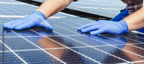 Male worker hands in glows on solar panel, technician installing solar panels on roof. Alternative energy sun energy power, ecological concept. Long web banner photo