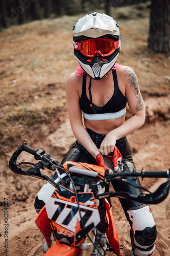 Fototapeta Modern young female motocross racer with pink hair in safety helmet riding on he