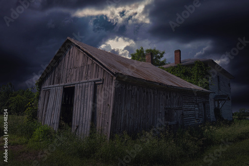 An abandoned farm house in rural Ontario with storm clouds looming in the background as shadows cast across the buildings.