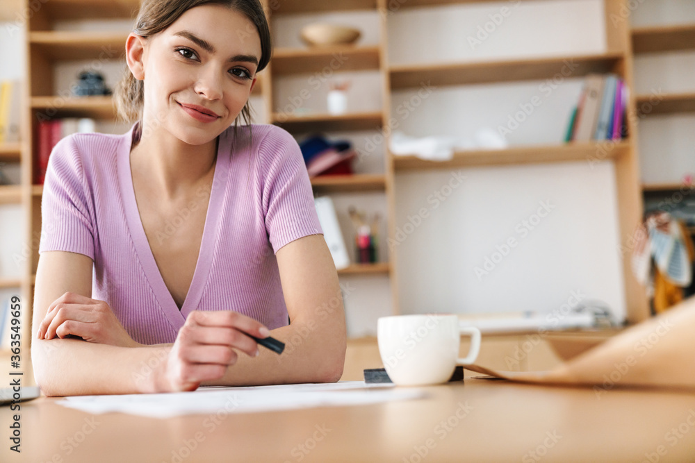 Photo of smiling woman making sketches while drinking coffee at table Photo of smiling woman making sketches while drinking coffee at table