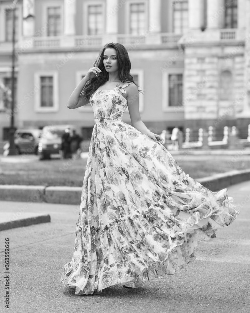 Outdoor fashion female portrait. Elegant woman in long ball gown dress. Caucaisan brunette woman with wavy hair. Girl walking city street