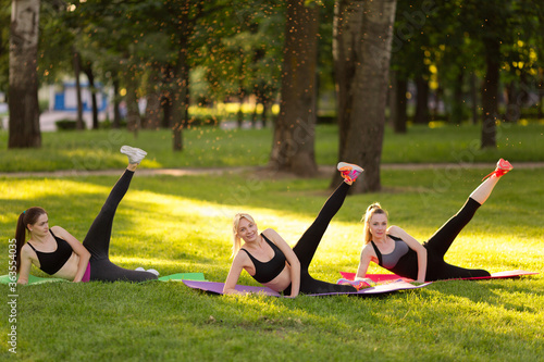  young people doing aerobics exercises together outdoors in a park tree women, in a healthy active lifestyle . meditate in the park, relaxation. Pretty woman practicing yoga on the grass