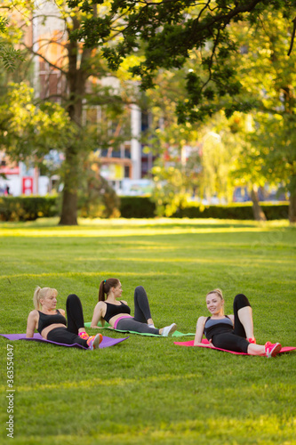  young people doing aerobics exercises together outdoors in a park tree women, in a healthy active lifestyle . meditate in the park, relaxation. Pretty woman practicing yoga on the grass