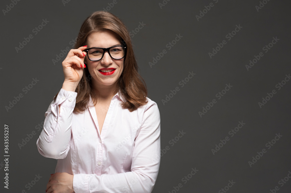 Happy smiling young woman wearing eyeglasses posing on grey background. Happy smiling young woman wearing eyeglasses posing on grey background.