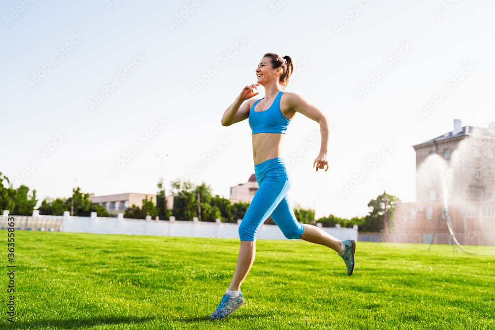 Young professional athlete woman practicing a run on stadium green grass on a sunny morning. Happy with her daily life. Every day increases the speed of her run