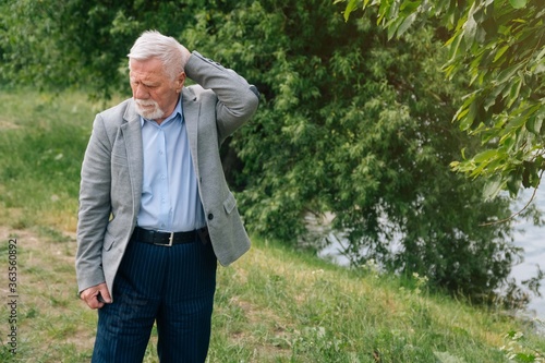 A brooding stylish old man in a business suit against the background of the forest.