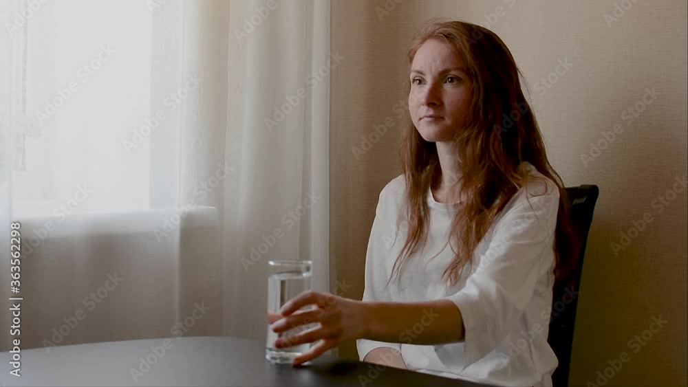 Positive young woman drinking water from glass talking with interlocutor. Happy caucasian woman in light kitchen at the house. Emotional conversation while having breakfast together in her apartment Positive young woman drinking water from glass talking with interlocutor. Happy caucasian woman in light kitchen at the house. Emotional conversation while having breakfast together in her apartment