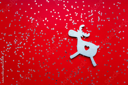View from above christmas silver wooden toy deer on red background with decorated silver stars. Copy space. Christmas and New Year greeting card
