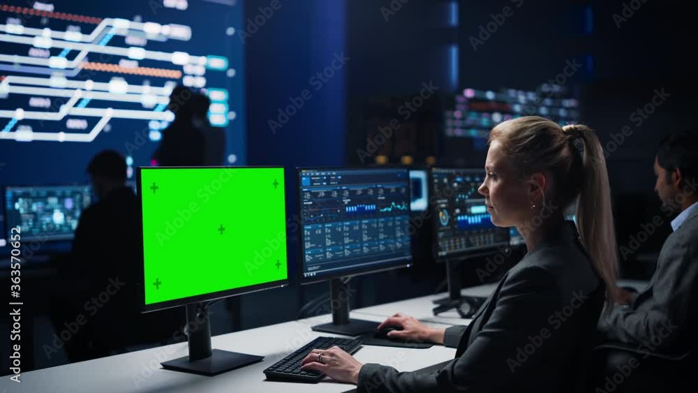 Confident Female Data Scientist Works on Green Chroma Key Screen Computer in Big Infrastructure Control Room. Specialists Use Computers Showing Graphs, Information. Control Room Professional Team Confident Female Data Scientist Works on Green Chroma Key Screen Computer in Big Infrastructure Control Room. Specialists Use Computers Showing Graphs, Information. Control Room Professional Team
