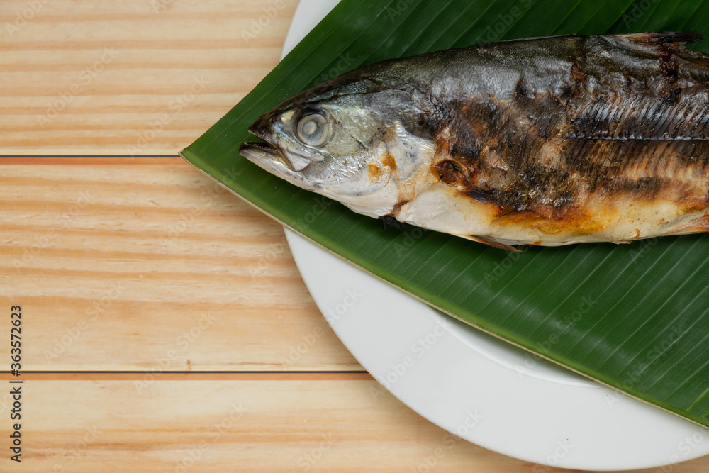 Close up grilled fish placed on banana leaf on a white plate with copy space.