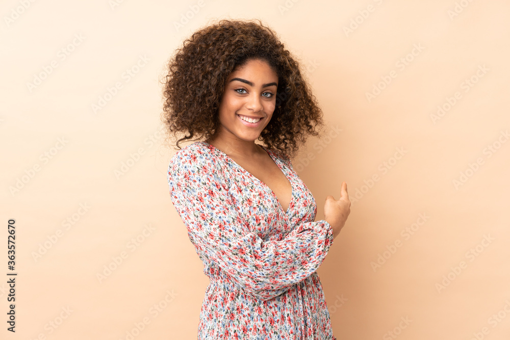 Young African American woman isolated on beige background pointing back Young African American woman isolated on beige background pointing back