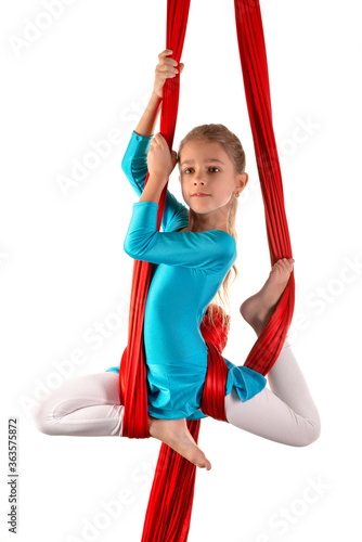 Cheerful pretty little girl in a blue gymnastic suit does tricks in a red air ribbon on a white background. Concept of children acrobats and gymnasts. Copyspace photo