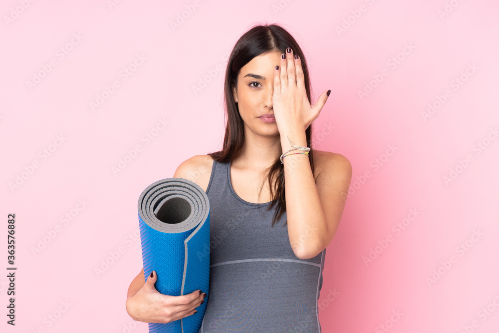 Young caucasian woman with mat isolated on pink background covering a eye by hand Young caucasian woman with mat isolated on pink background covering a eye by hand