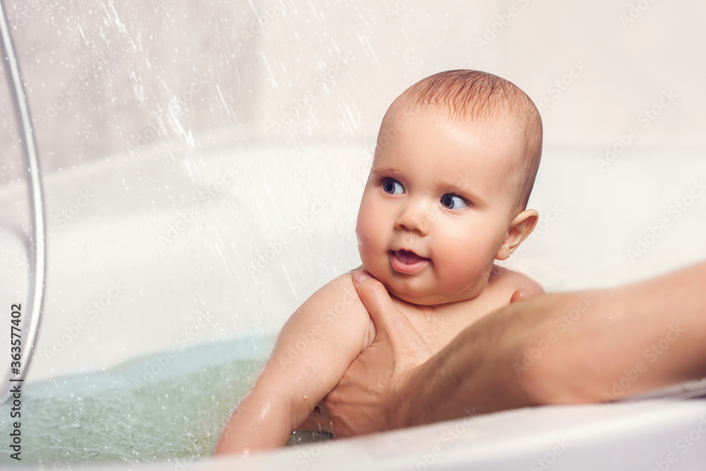 Hands of a careful unknown mother hold a small beautiful funny big-eyed baby. The concept of care and hygiene over children.